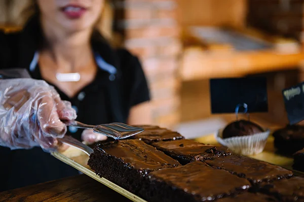 Female Shop Assistant Selling Chocolate Cake In Bakery